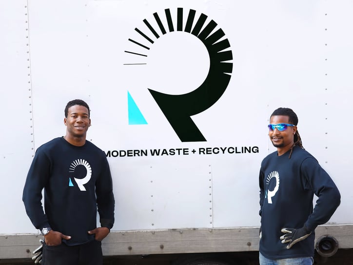 Two truck drivers smiling in front of a box truck with a roadrunner logo